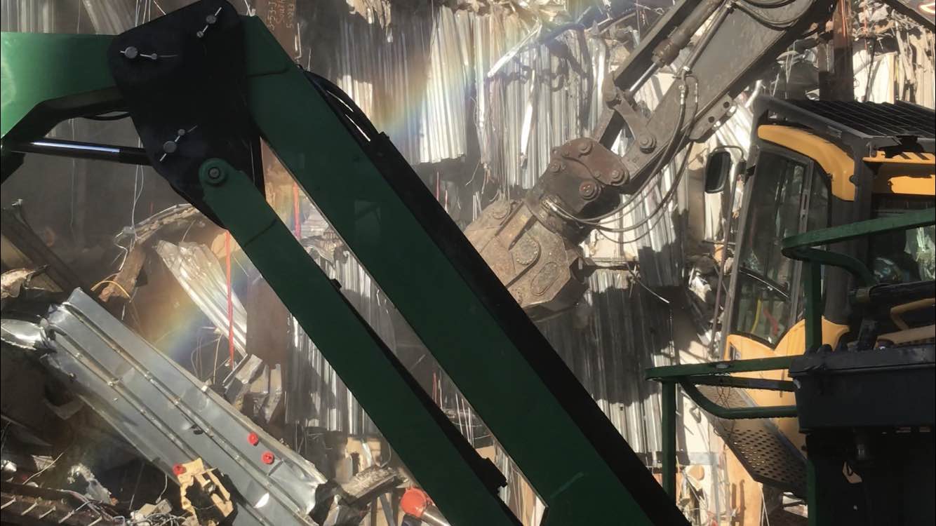 A demolition site showing  corrugated metal chutes with the arms of metal cranes in the foreground